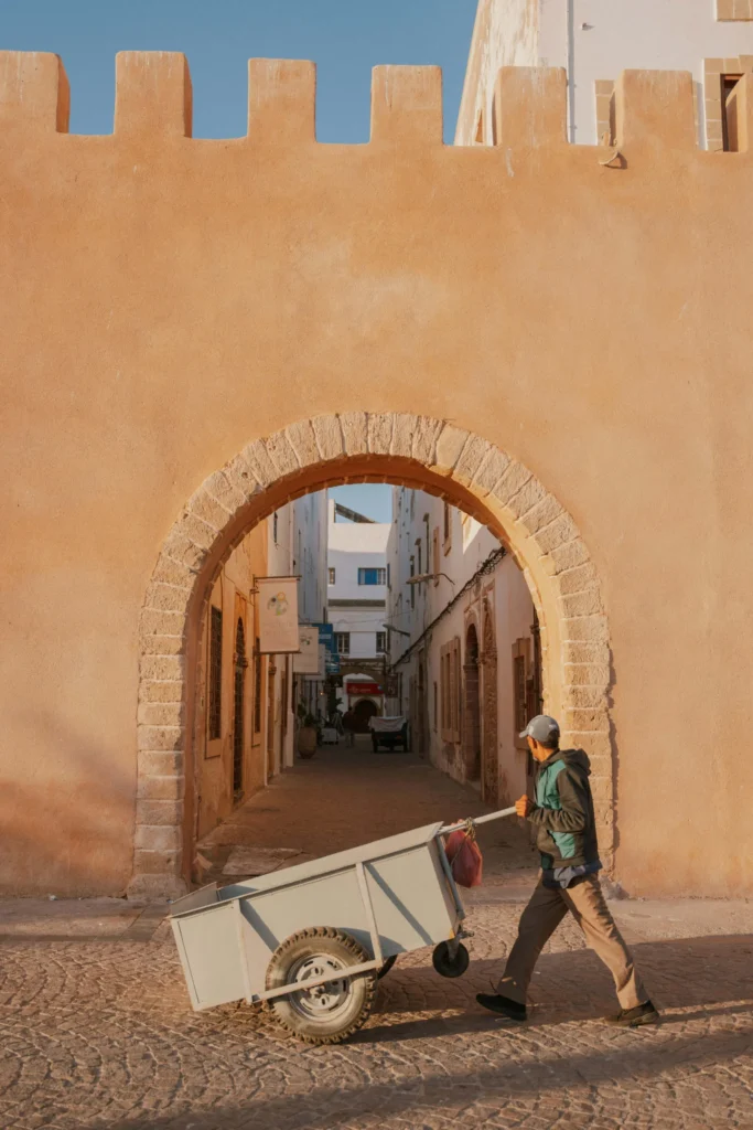 Man pushing a cart through an arched entrance in Essaouira’s medina, showcasing traditional Moroccan architecture.