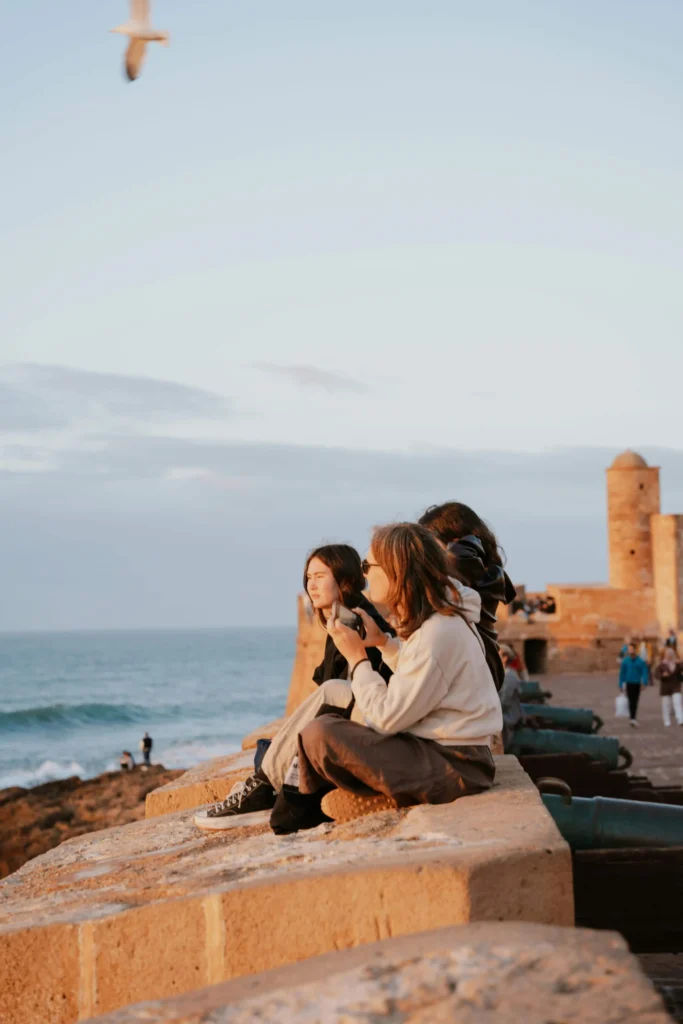 Tourists enjoying the sunset while sitting on the seawall near Essaouira’s historic fortifications.